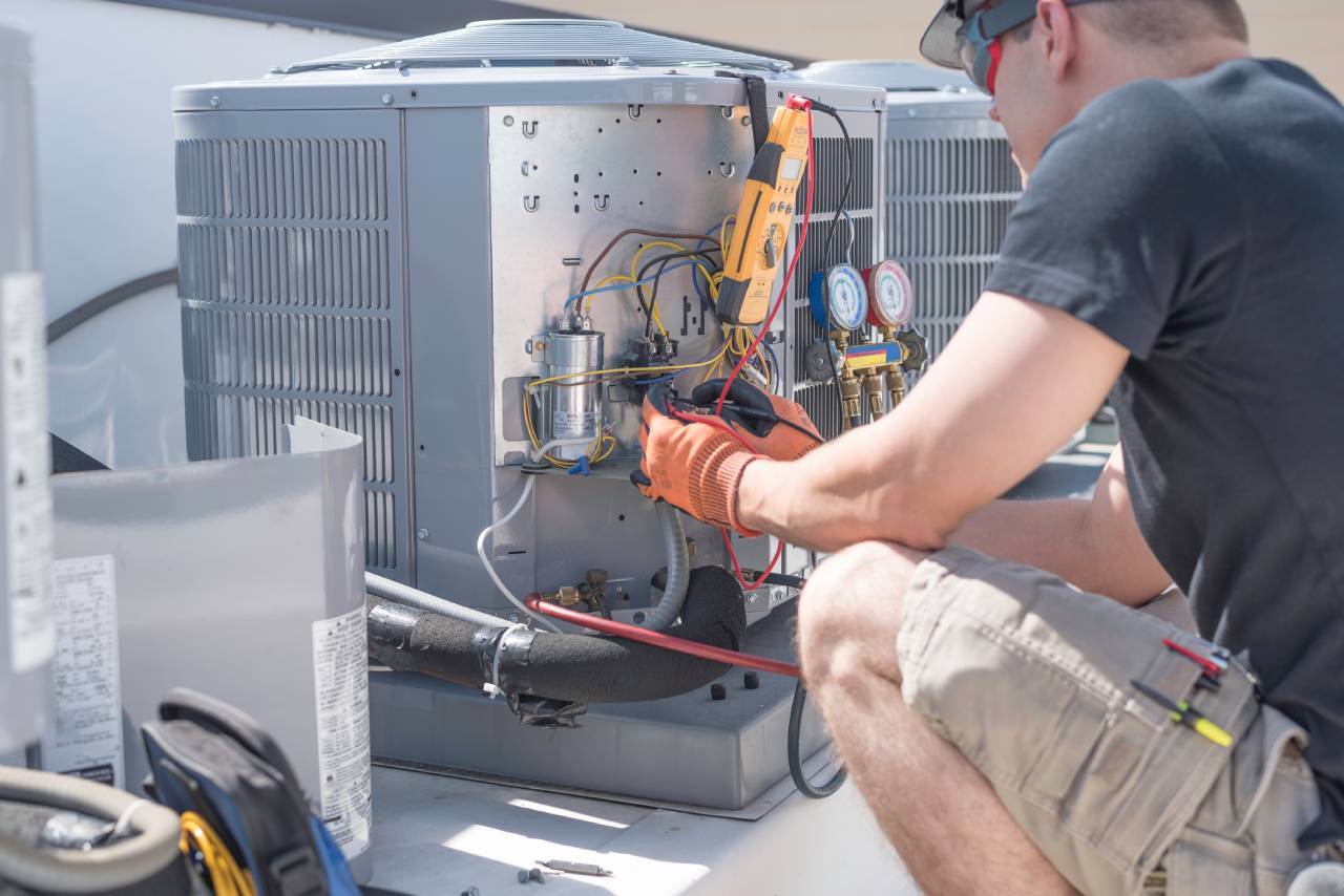 Technician repairs an air conditioning unit, using tools and wearing protective gloves.