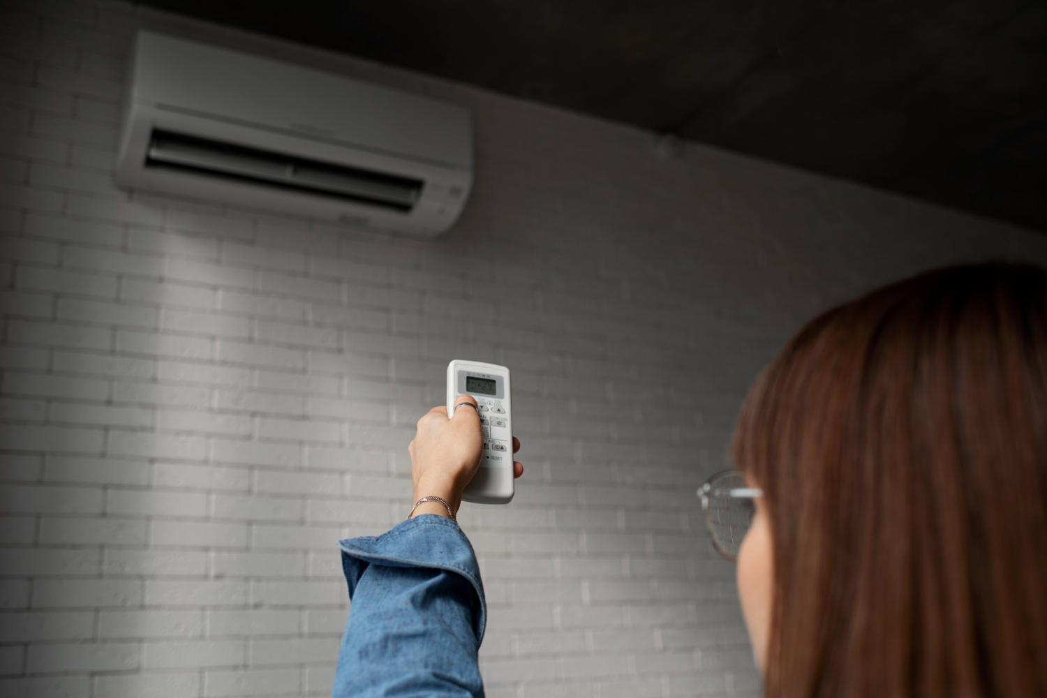 Person holding a remote control up towards a wall-mounted air conditioner in a modern room.