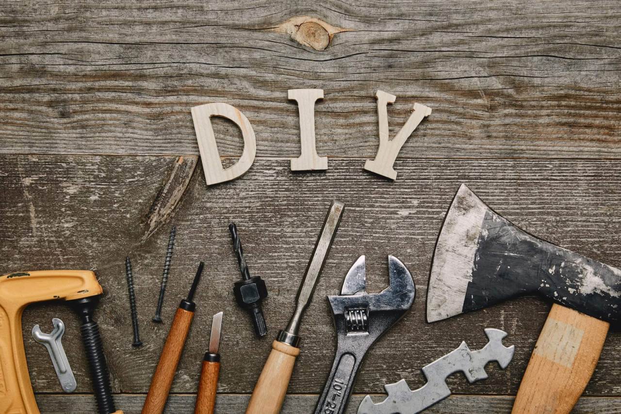 Wooden letters spelling "DIY" surrounded by various hand tools on a wooden surface.