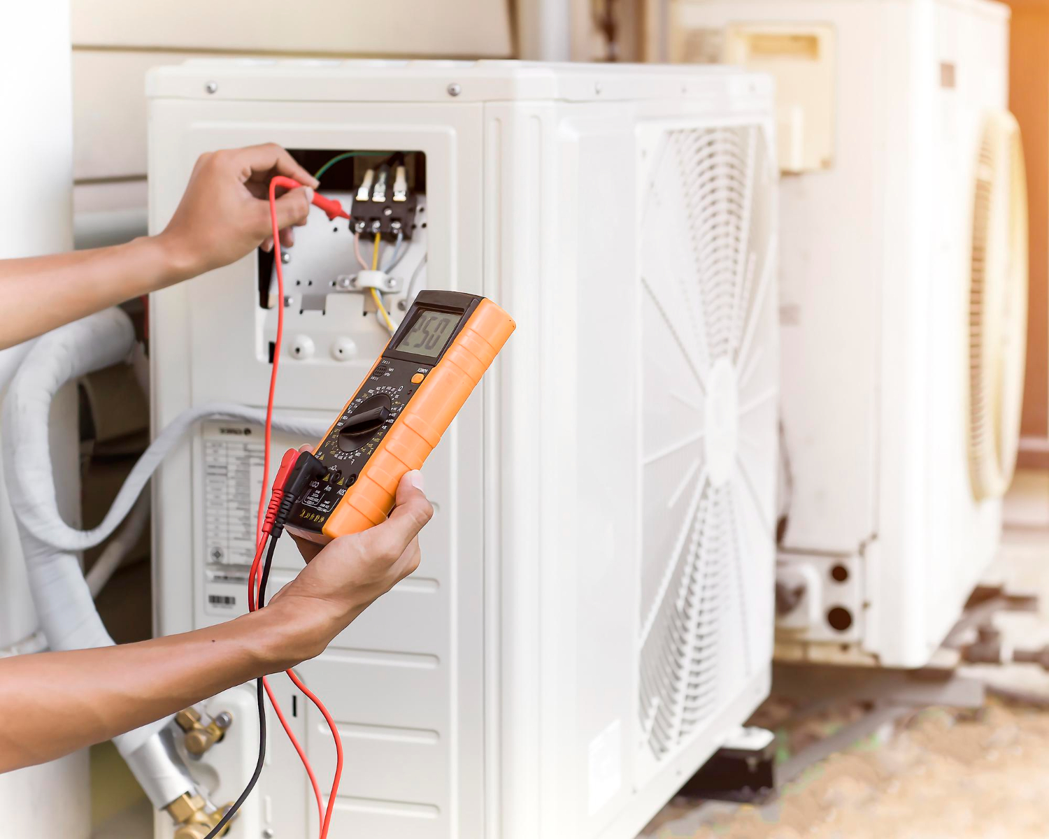 Technician tests an air conditioning unit using a multimeter outdoors.